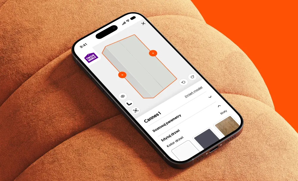 TwojeMeble wardrobe configurator on a phone resting on an orange sofa